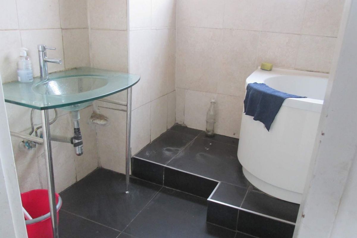 A compact bathroom featuring a glass pedestal sink, raised platform area, and tiled finishes, requiring some maintenance and cosmetic updates.