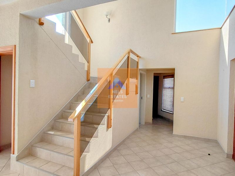 Spacious entrance hall featuring a tiled staircase with a modern glass balustrade and double volume ceilings, creating an open and airy atmosphere.