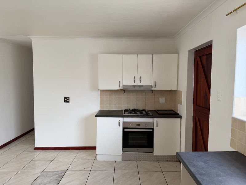 A compact kitchen featuring white cabinetry, a gas hob, built-in oven, extractor fan, and tiled flooring, presenting a functional and clean layout.
