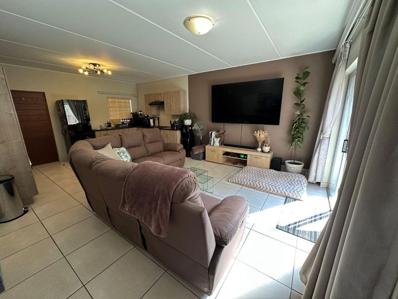 Open-plan living area featuring tiled flooring, a sliding door to the exterior, and an integrated kitchen space with wooden cabinetry.