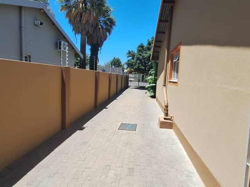 A paved side passage or driveway area featuring a high boundary wall, security gate, and functional drainage.