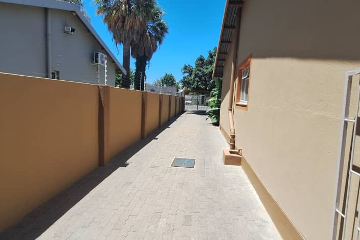 A paved side passage or driveway area featuring a high boundary wall, security gate, and functional drainage.