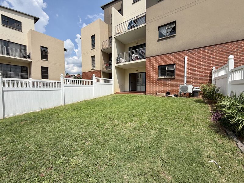 A private rear garden area featuring a lawn, white vinyl fencing, and access to the apartment building's lower level via sliding glass doors.