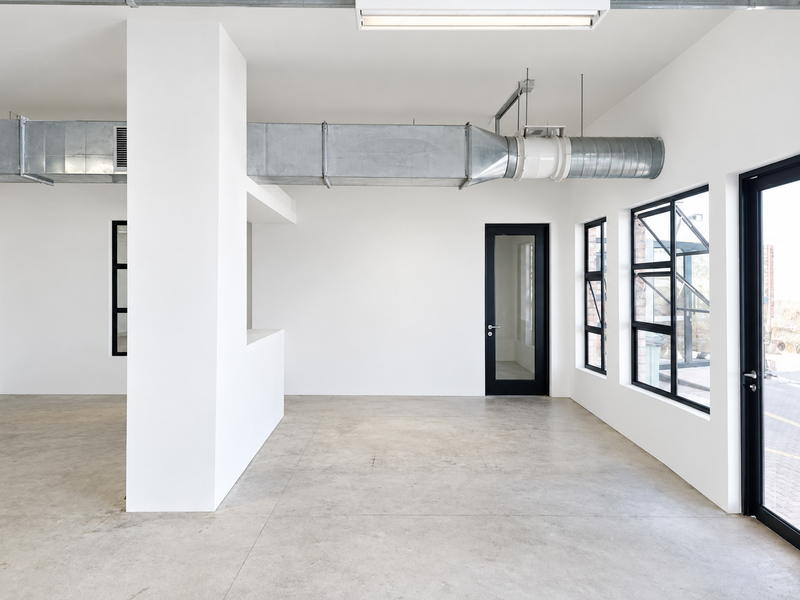A bright, modern open-plan industrial space featuring polished concrete floors, exposed HVAC ducting, and large black-framed windows providing ample natural light.