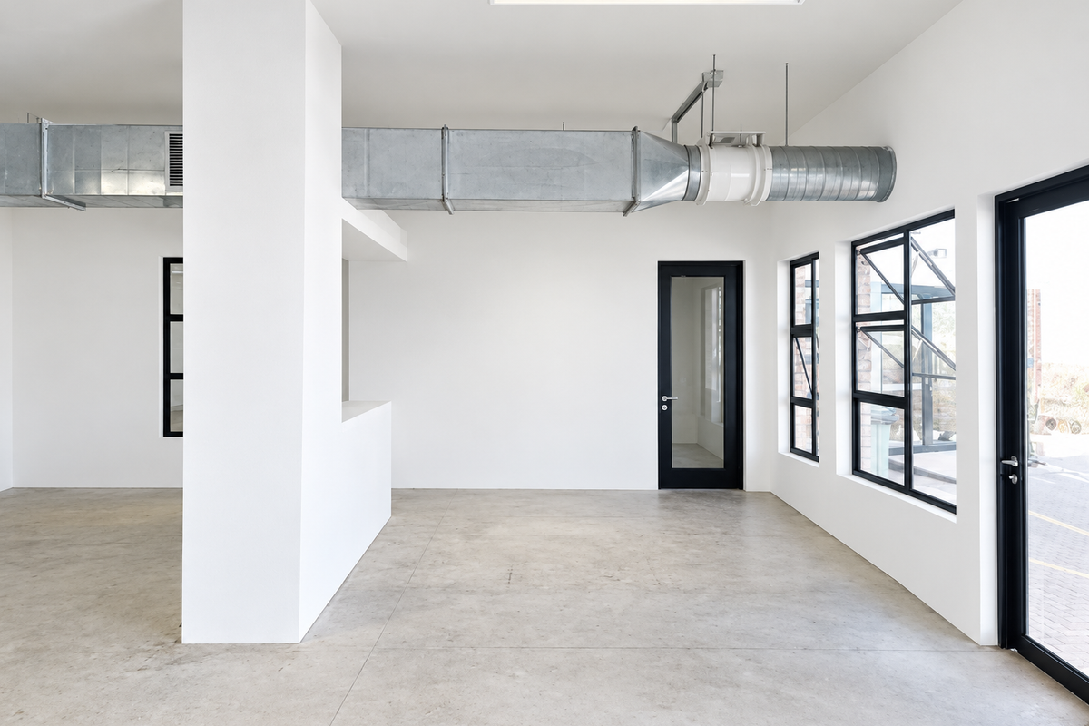 A bright, modern open-plan industrial space featuring polished concrete floors, exposed HVAC ducting, and large black-framed windows providing ample natural light.