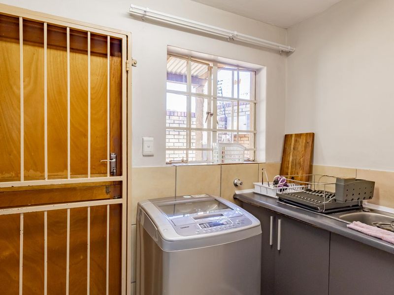 Functional laundry area featuring built-in cabinetry, a stainless steel sink with mixer tap, and a secure exterior door with burglar bars.
