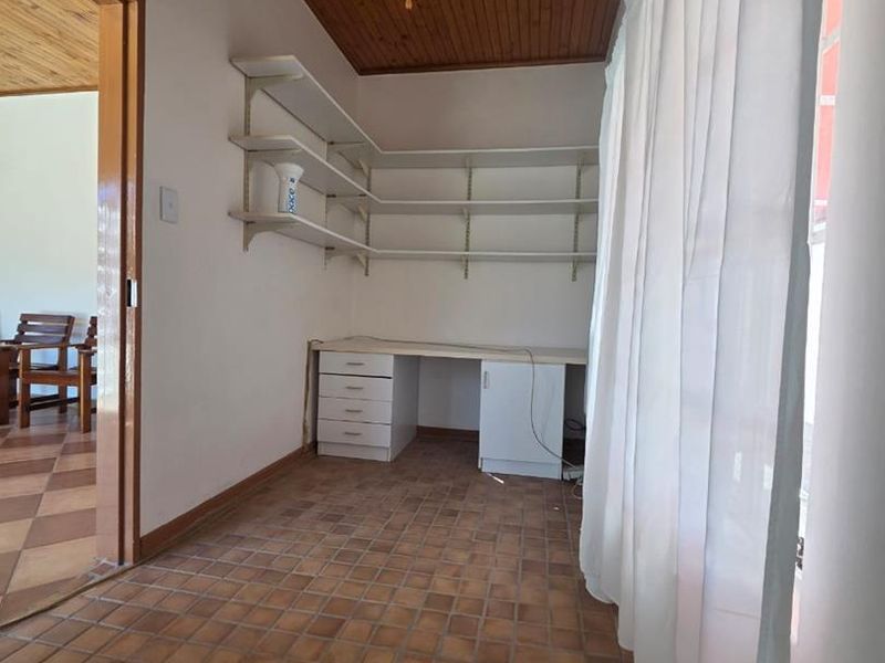A functional home office space featuring built-in desk and shelving, timber ceiling, ceiling fan, and tiled flooring.