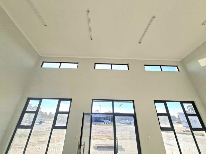 A bright, open-plan office space featuring high ceilings, large aluminium-framed windows, and glass entrance doors, offering a clean and modern professional environment.
