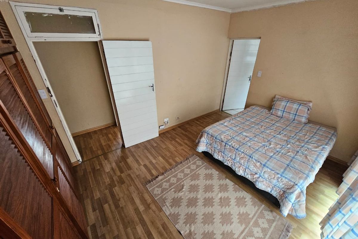 A bedroom featuring wood-look laminate flooring, built-in wooden cabinetry, and neutral wall finishes with access to adjacent rooms.