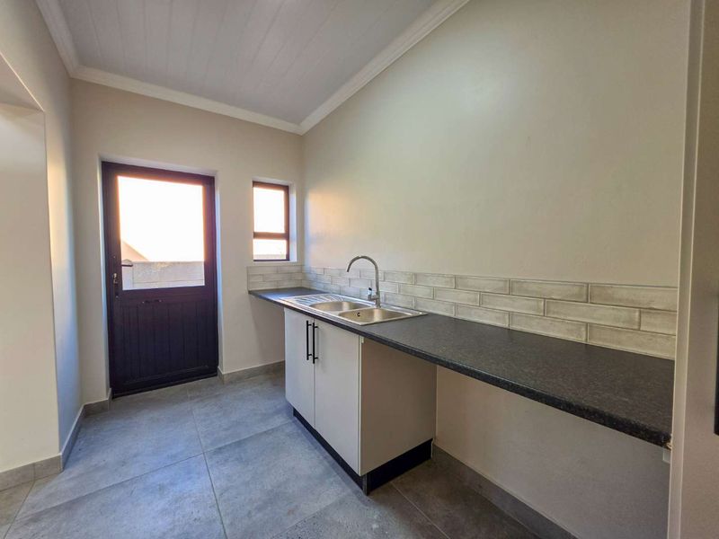 A clean and functional scullery featuring a stainless steel sink, modern subway tile backsplash, dark laminate countertops, and direct access to the exterior.