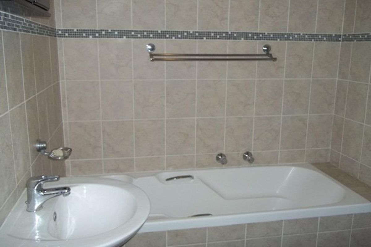A functional bathroom featuring a built-in bathtub, pedestal basin, chrome fixtures, and neutral wall tiling with a decorative mosaic border.