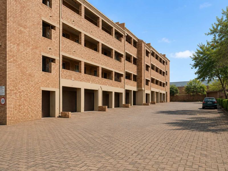 Exterior view of a multi-story apartment complex featuring face-brick facade, ground-level garages, and paved driveway area.