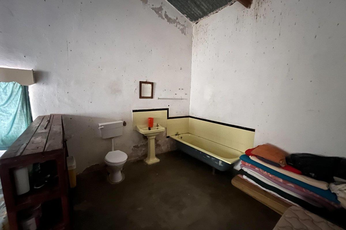 A rustic bathroom featuring a vintage pedestal sink, a built-in bathtub, and a toilet, requiring significant renovation and cosmetic updates.