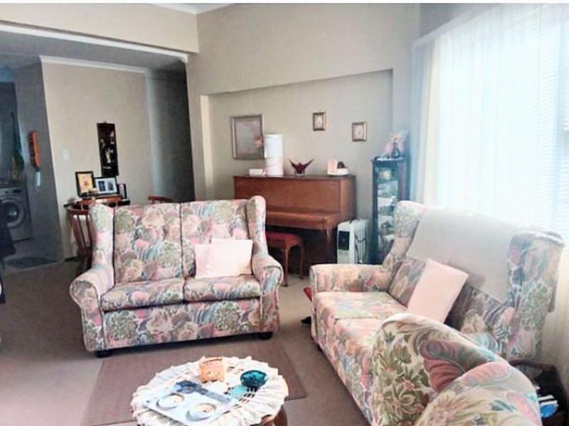 A living room area featuring neutral wall tones, coving, and a large window allowing for natural light.