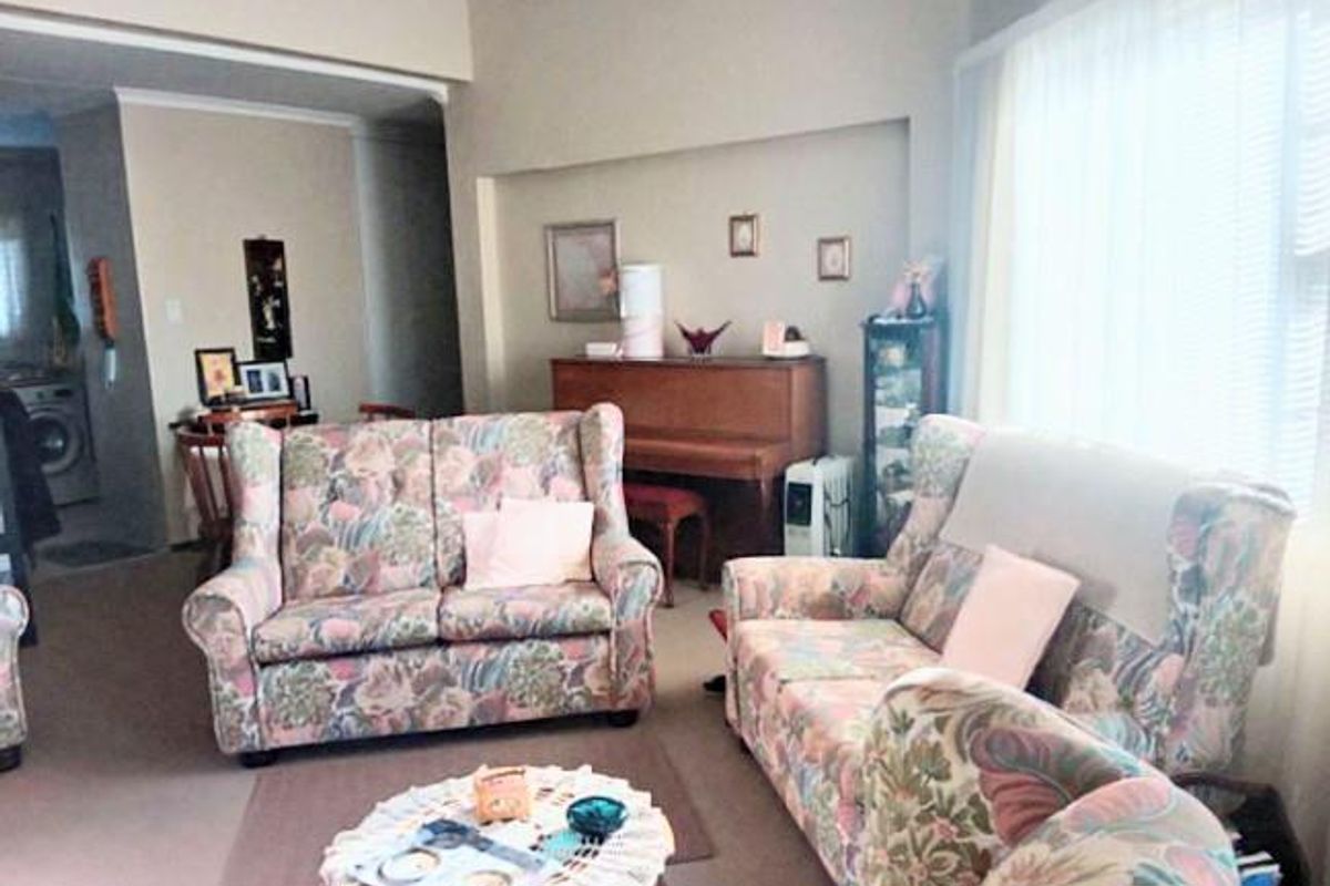 A living room area featuring neutral wall tones, coving, and a large window allowing for natural light.