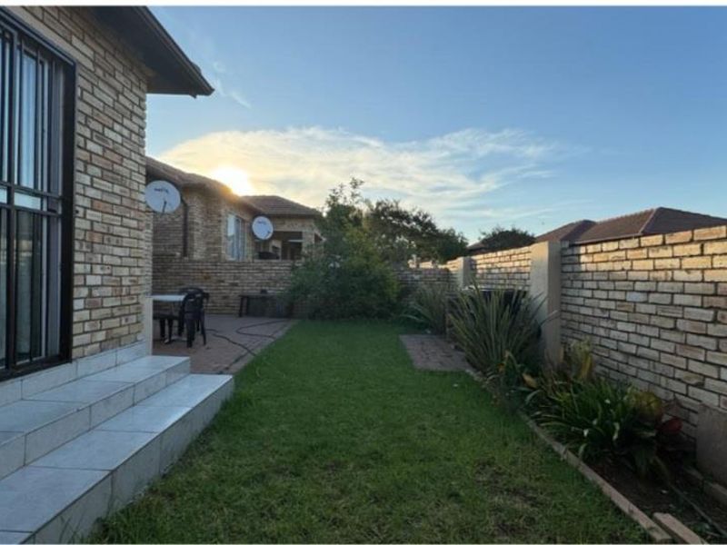 A private rear garden featuring a paved patio area, tiled steps leading to the home, and a well-maintained lawn enclosed by face brick boundary walls.