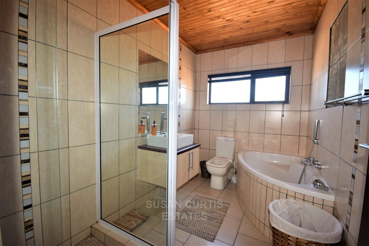 A functional bathroom featuring a corner bathtub, separate shower enclosure, vessel sink vanity, and timber ceiling with neutral wall tiling.