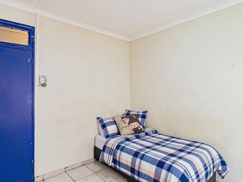 A compact bedroom featuring tiled flooring and a blue door, requiring cosmetic updates to the wall finishes to improve the overall aesthetic.