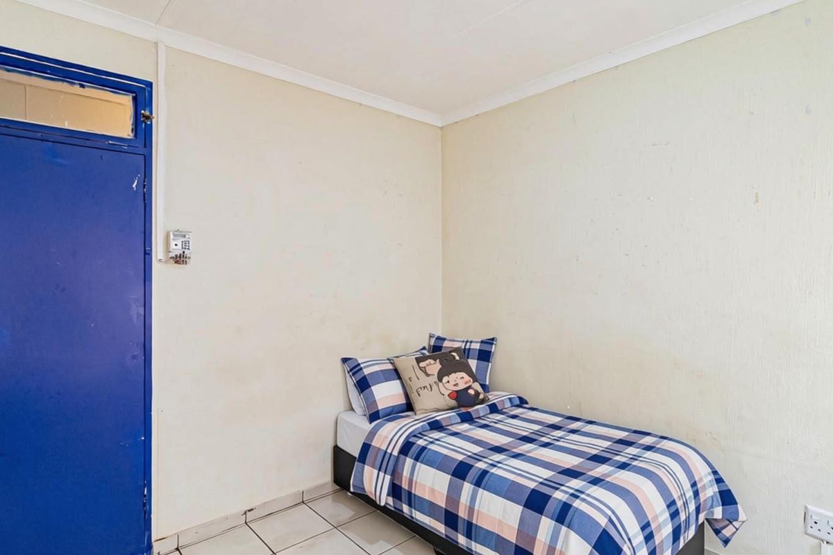A compact bedroom featuring tiled flooring and a blue door, requiring cosmetic updates to the wall finishes to improve the overall aesthetic.