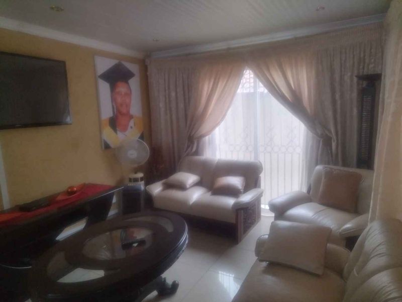 A living room featuring tiled flooring, coved ceilings, and a sliding glass door with an integrated security gate, providing access to the exterior.