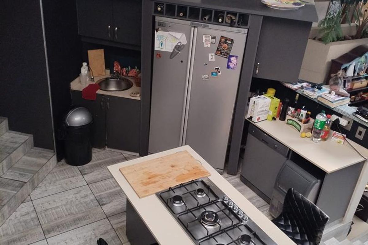A functional kitchen featuring dark cabinetry, a central island with a built-in gas hob, tiled flooring, and integrated storage solutions.