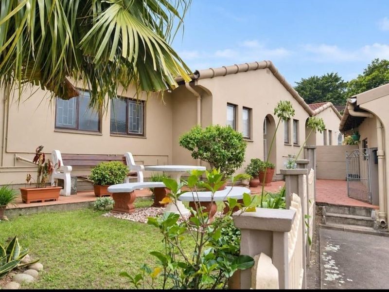 A well-maintained rear exterior view of the townhouse featuring a paved patio area, small garden, and secure perimeter fencing.