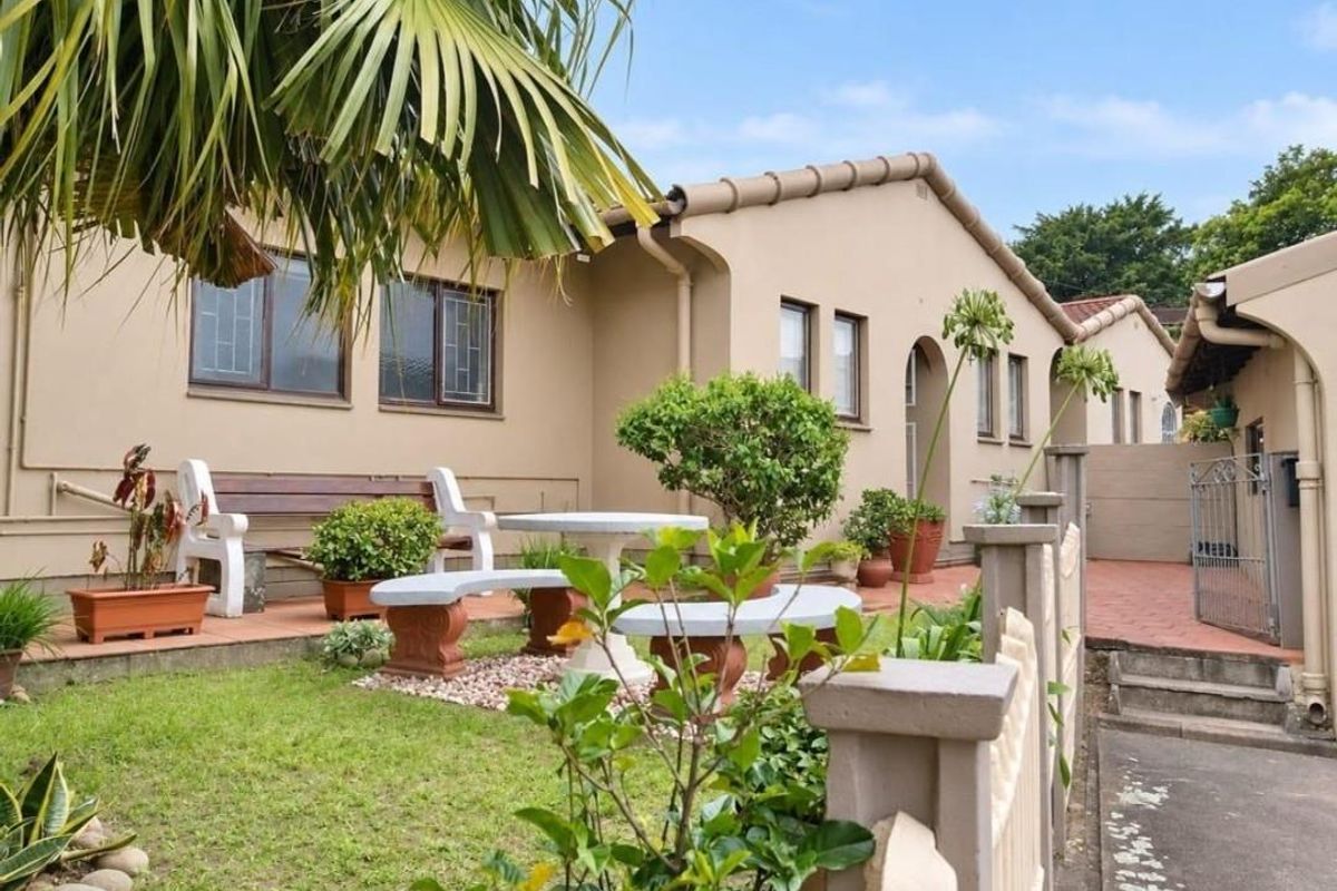 A well-maintained rear exterior view of the townhouse featuring a paved patio area, small garden, and secure perimeter fencing.