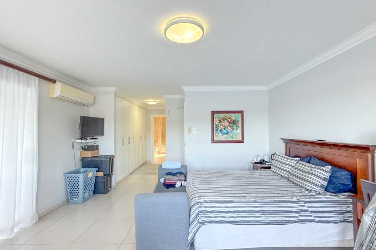Spacious bedroom featuring tiled flooring, built-in cupboards, crown molding, and an integrated air conditioning unit, with direct access to an en-suite bathroom.