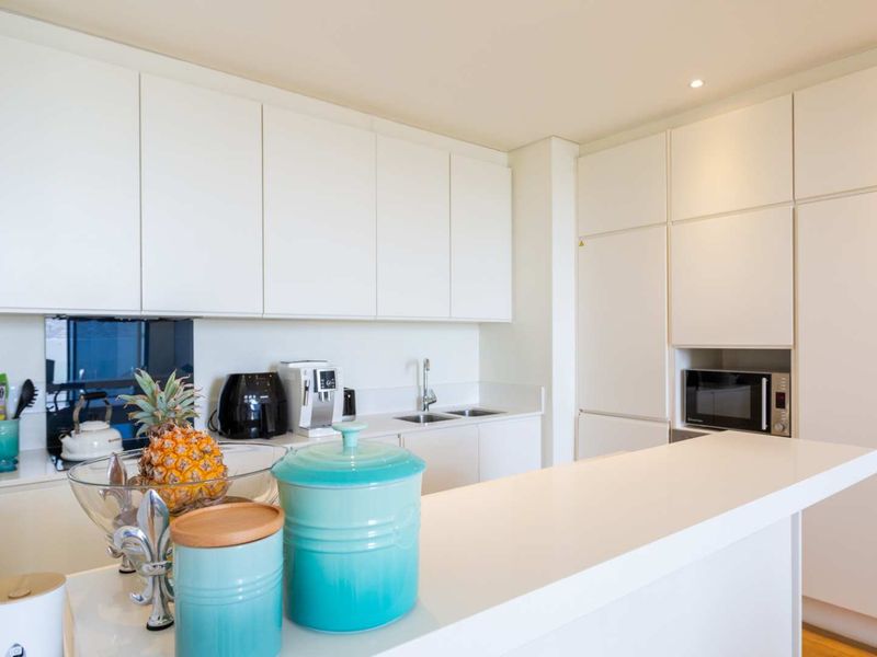 Modern kitchen featuring sleek white cabinetry, integrated appliances, a double sink, and a functional breakfast bar for casual dining.