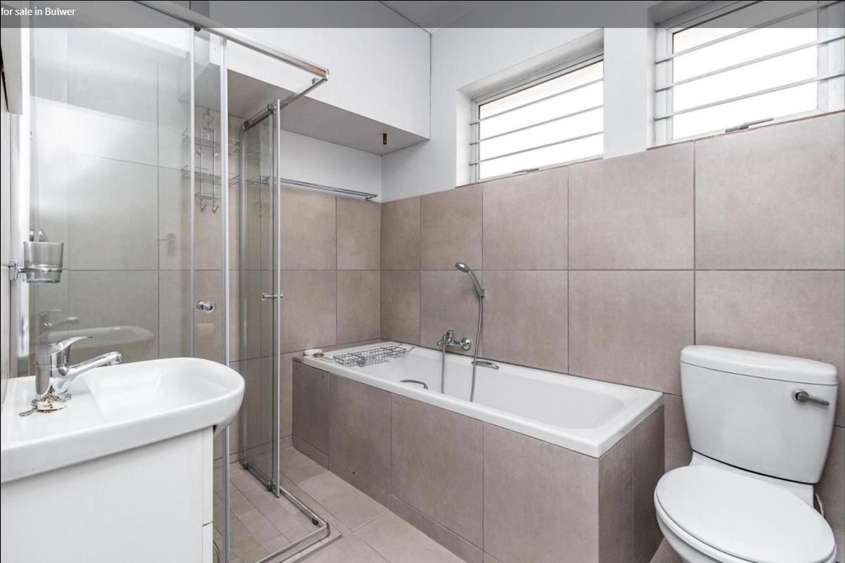 Modern bathroom featuring a glass shower enclosure, built-in bathtub, pedestal washbasin, and neutral ceramic tiling throughout.