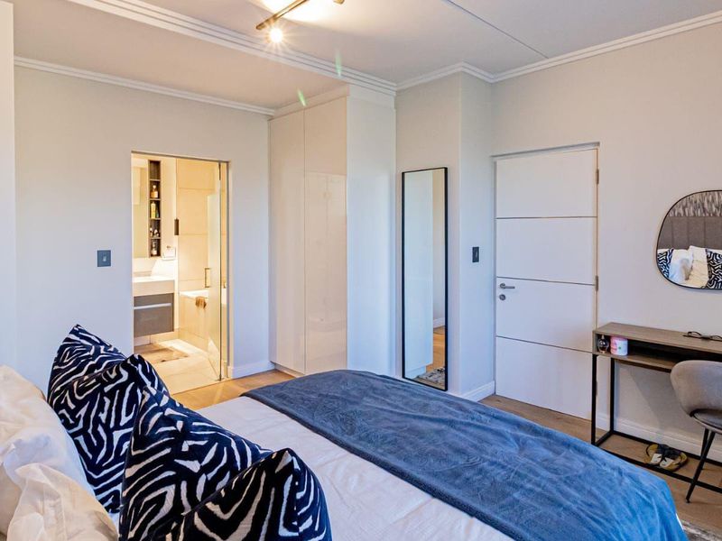 A well-maintained bedroom featuring built-in wardrobes, laminate flooring, and direct access to an en-suite bathroom with modern finishes.
