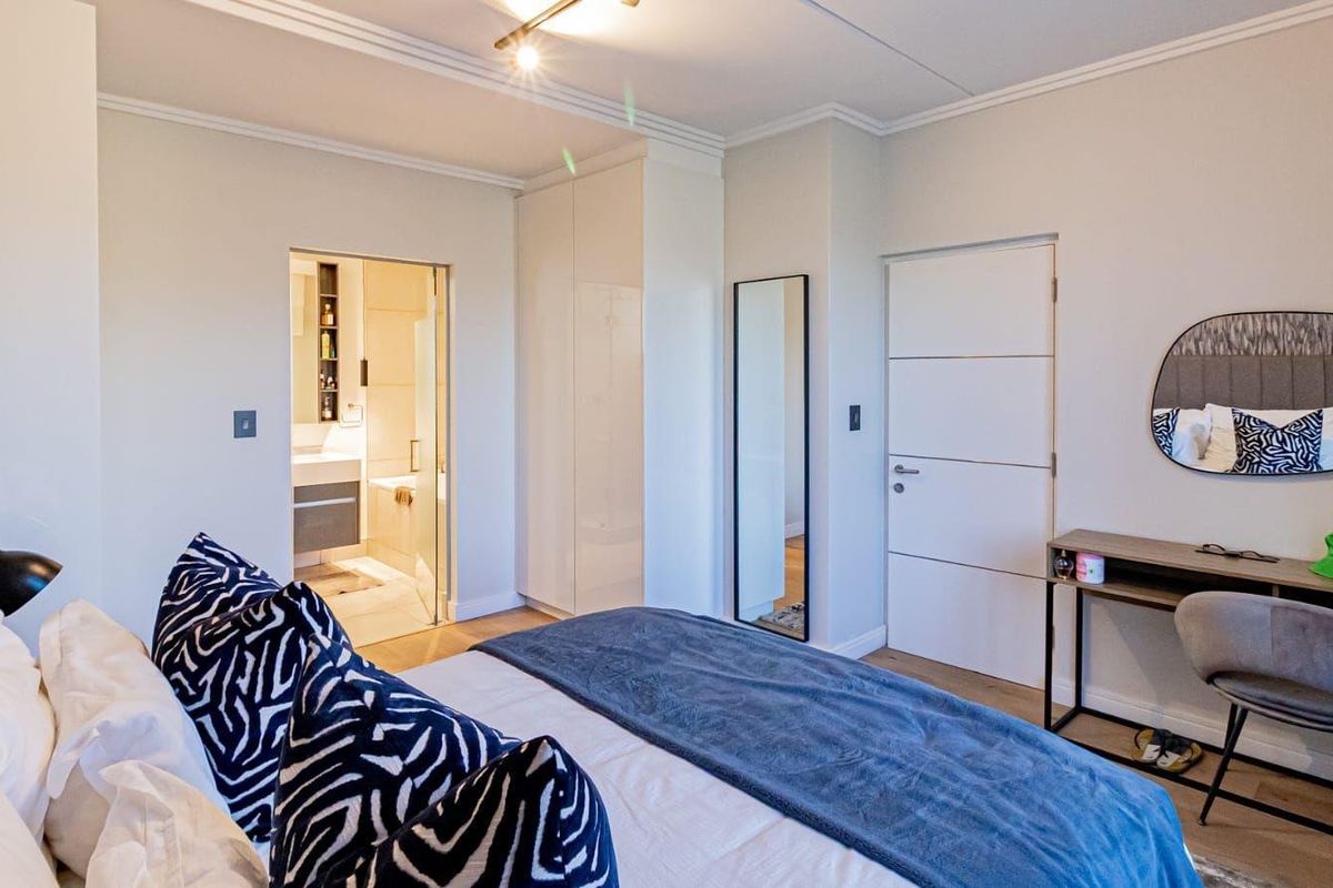 A well-maintained bedroom featuring built-in wardrobes, laminate flooring, and direct access to an en-suite bathroom with modern finishes.