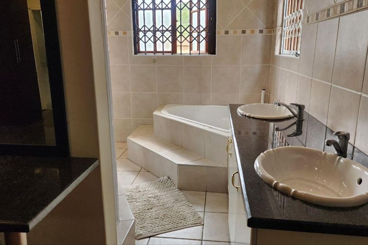 A spacious bathroom featuring a raised corner bathtub, dual vanity with granite countertops, and security bars on the windows.