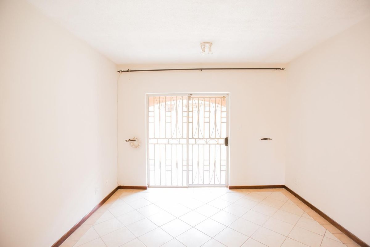 An empty living room featuring tiled flooring and a sliding glass door with a security gate leading to the exterior.