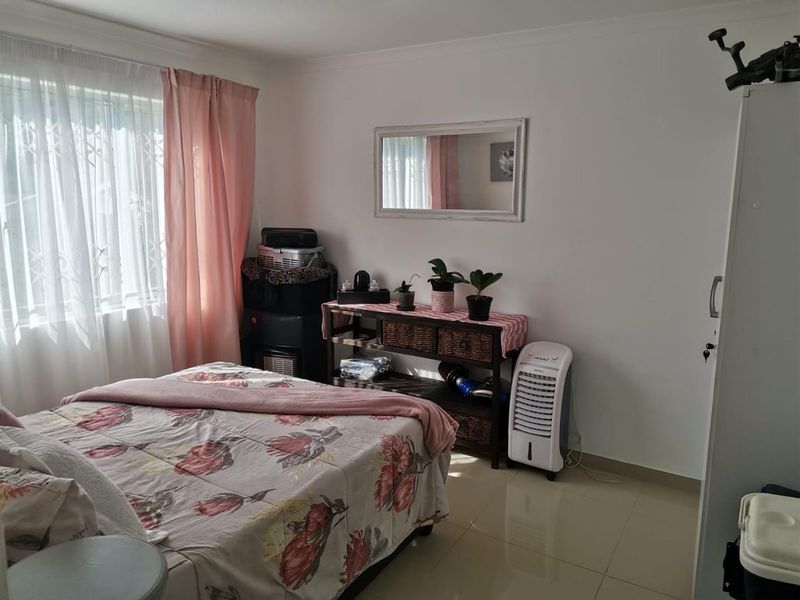 A well-lit bedroom featuring neutral tiled flooring, a window with security bars, and classic cove cornicing, offering a clean and functional living space.