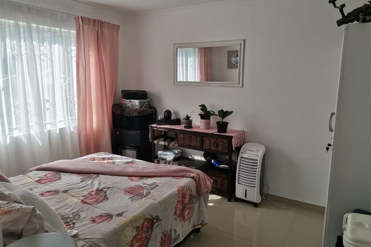 A well-lit bedroom featuring neutral tiled flooring, a window with security bars, and classic cove cornicing, offering a clean and functional living space.