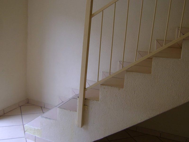 A simple interior staircase featuring tiled steps and a metal balustrade, showing signs of wear and dated finishes.
