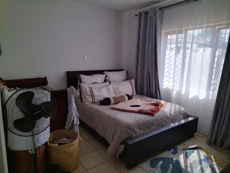A functional bedroom featuring tiled flooring and a large window with curtain tracks, providing natural light and a comfortable living space.