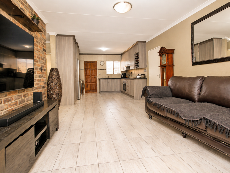 Spacious open-plan living area featuring a brick accent wall, tiled flooring, and a modern kitchen with built-in cabinetry and integrated appliances.