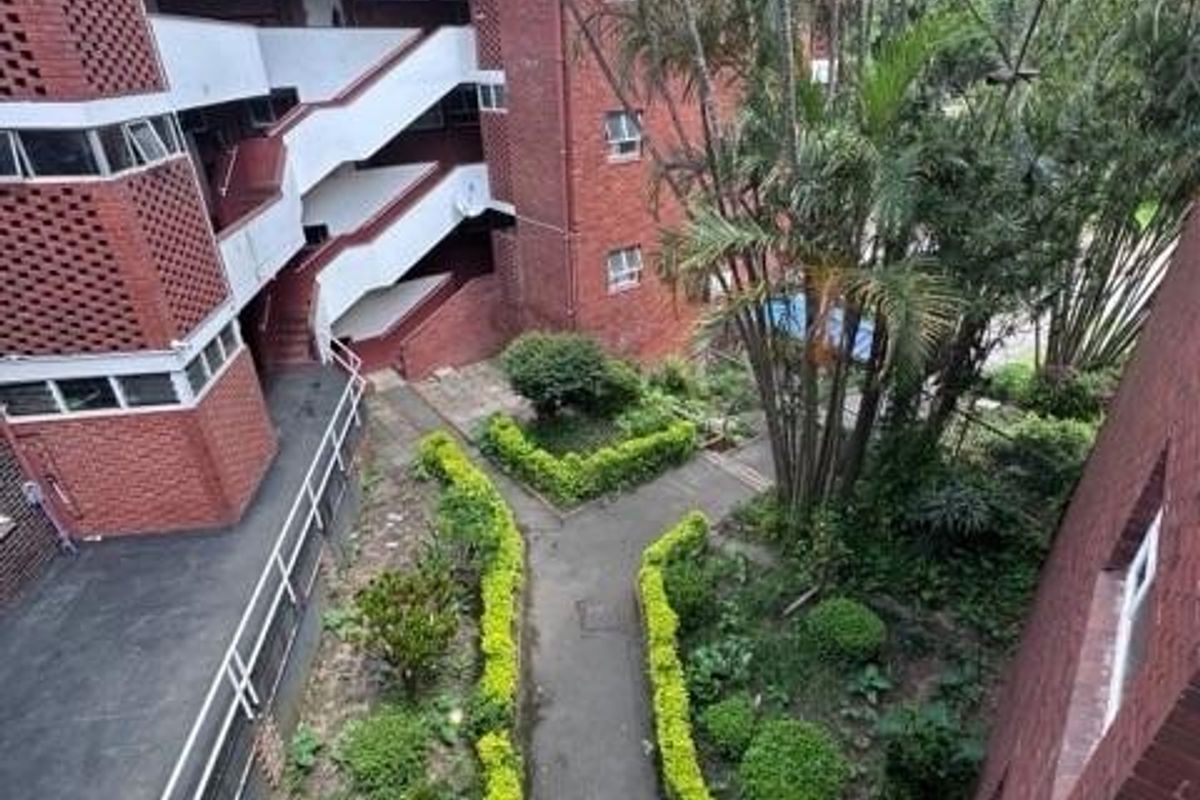 Elevated view of a townhouse complex exterior featuring red brick architecture, external staircases, and a landscaped garden pathway.