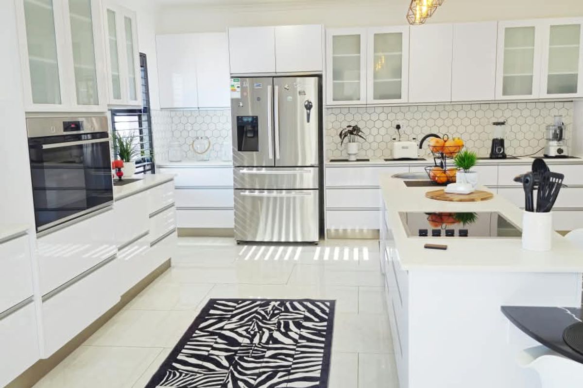 Modern, bright kitchen featuring white cabinetry, a central island with a built-in cooktop, high-end appliances, and a stylish hexagonal tiled backsplash.