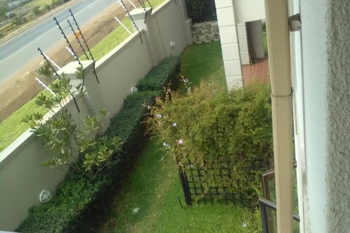 An elevated view of the apartment's side garden area, featuring perimeter walling with electric fencing and established landscaping.