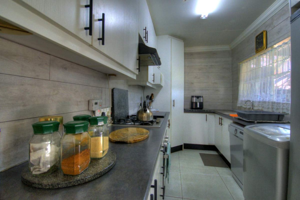 A functional kitchen featuring white cabinetry, dark countertops, a built-in gas hob, extractor fan, and tiled flooring.