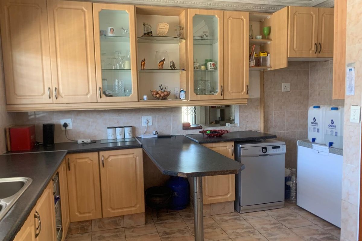 A functional kitchen featuring light wood-tone cabinetry, dark laminate countertops, tiled backsplash, and tiled flooring with an integrated dishwasher.