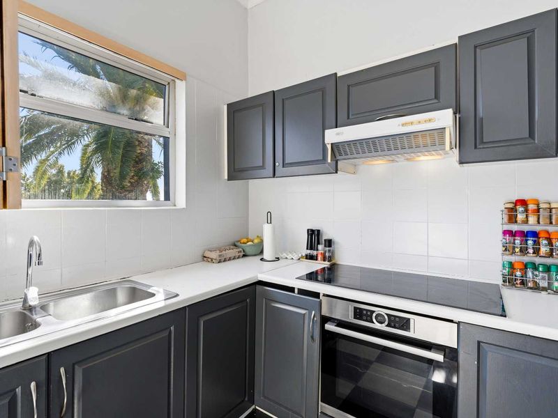 A functional kitchen featuring dark grey cabinetry, a built-in oven with electric cooktop, extractor fan, and a stainless steel sink with tiled backsplash.