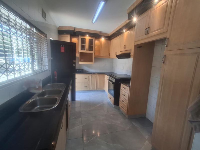A functional kitchen featuring light wood cabinetry, dark granite countertops, tiled flooring, and a double bowl stainless steel sink with an integrated oven.