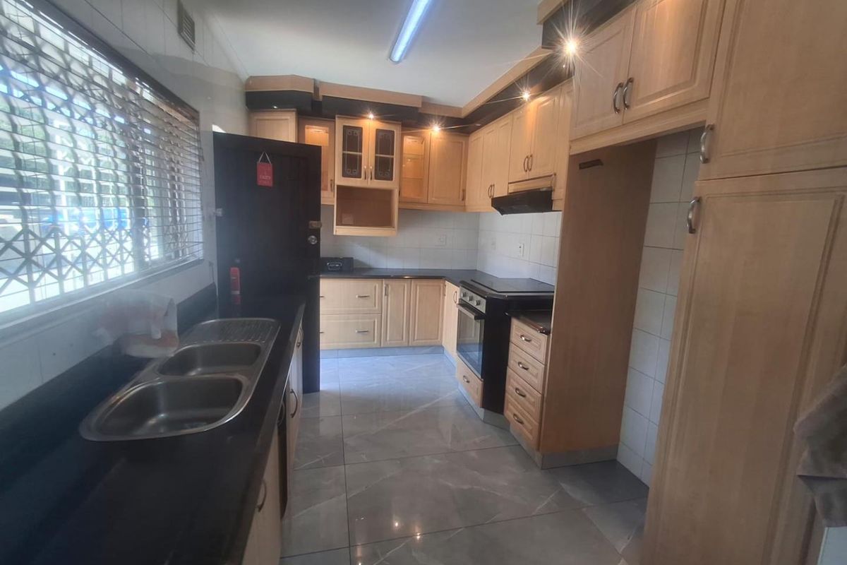 A functional kitchen featuring light wood cabinetry, dark granite countertops, tiled flooring, and a double bowl stainless steel sink with an integrated oven.