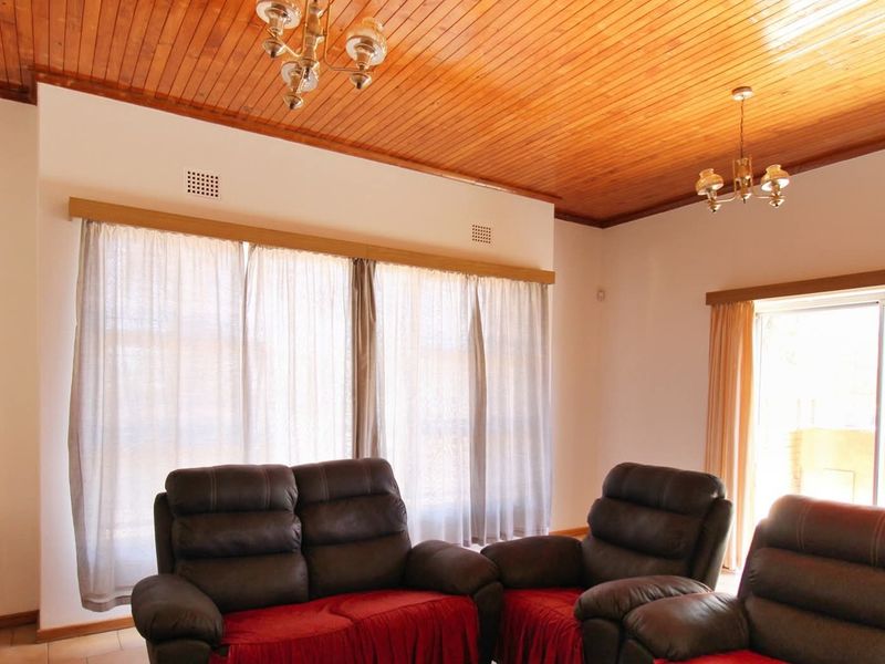 Spacious living room featuring a warm timber tongue and groove ceiling, tiled flooring, and large windows providing natural light with access to the patio.