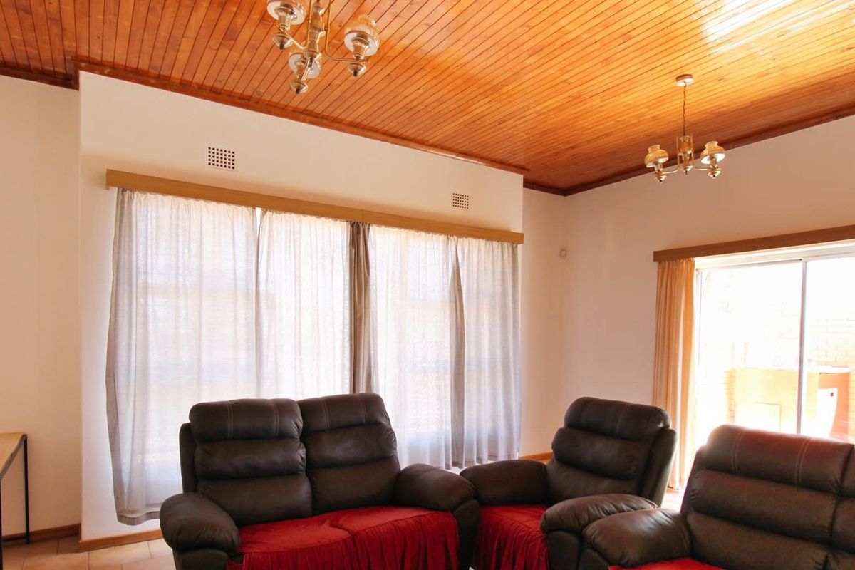 Spacious living room featuring a warm timber tongue and groove ceiling, tiled flooring, and large windows providing natural light with access to the patio.