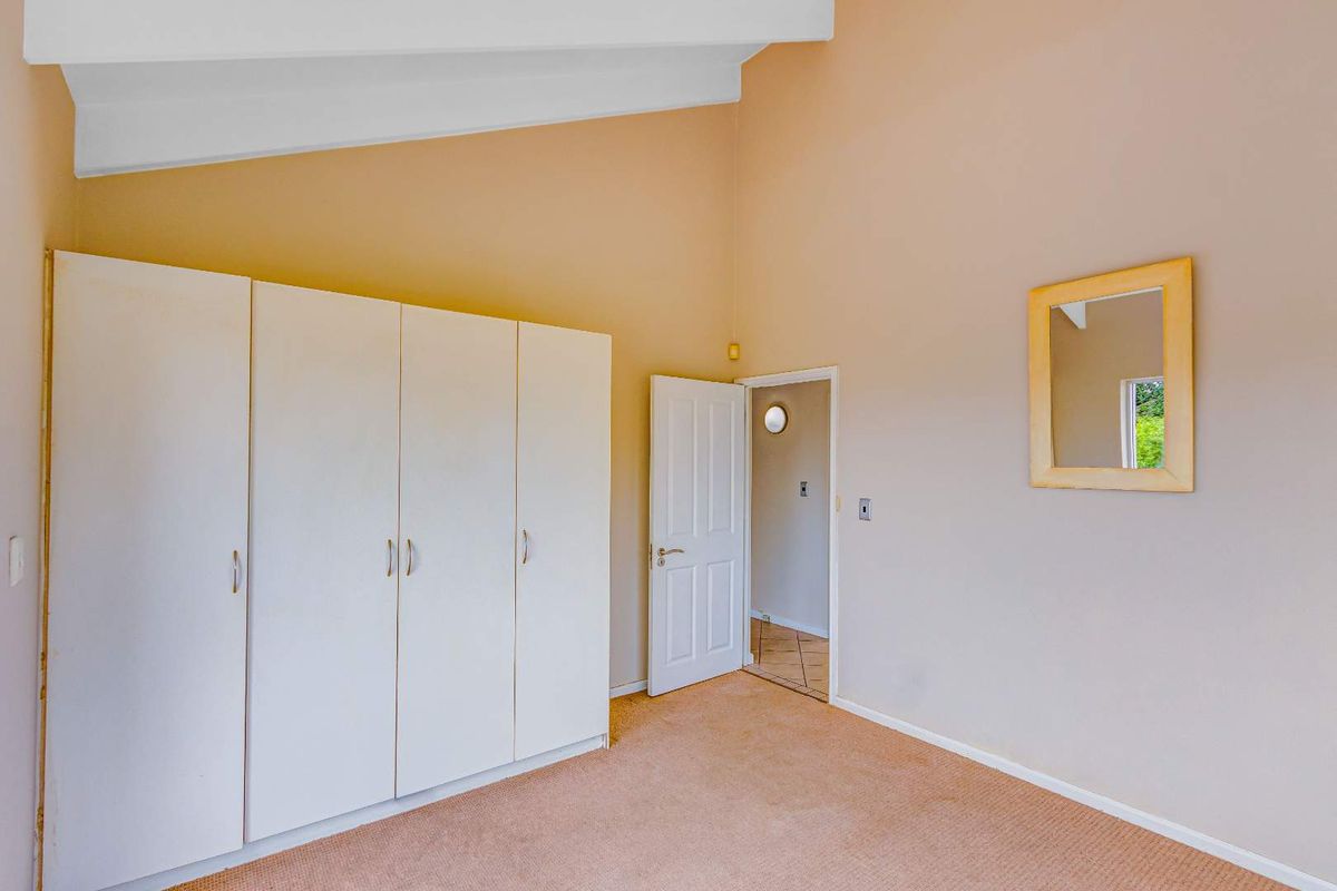 A bedroom featuring high vaulted ceilings, built-in white cabinetry, and neutral carpeting, with an adjacent doorway leading to a hallway.